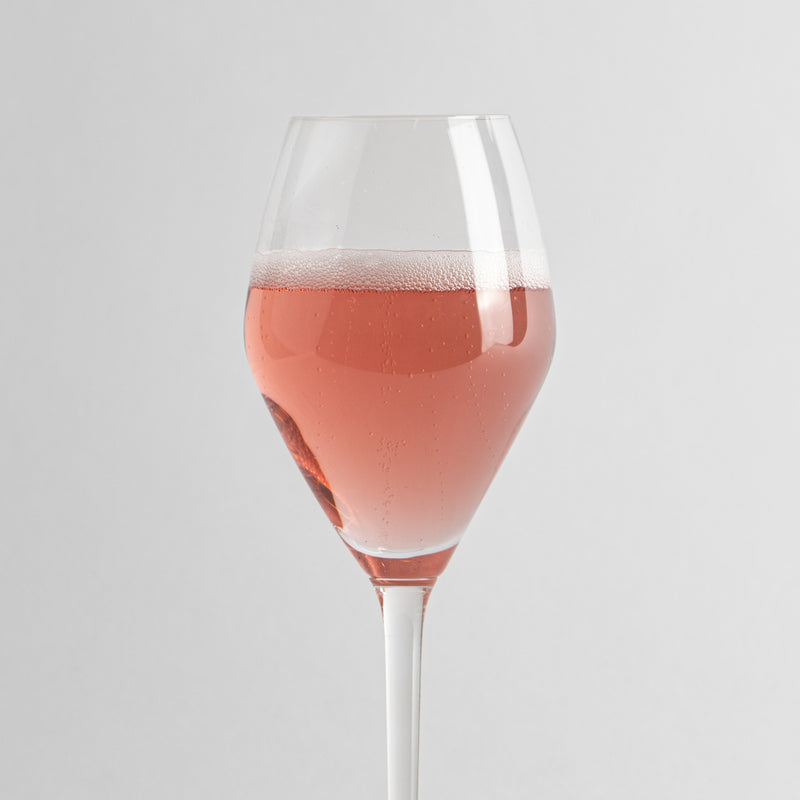bicchiere di vetro trasparente a calice con liquido rosa frizzante su sfondo grigio chiaro