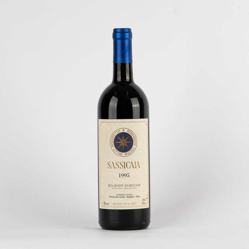 Botella de vino tinto Sassicaia 1995 con etiqueta beige y tapón azul sobre fondo blanco