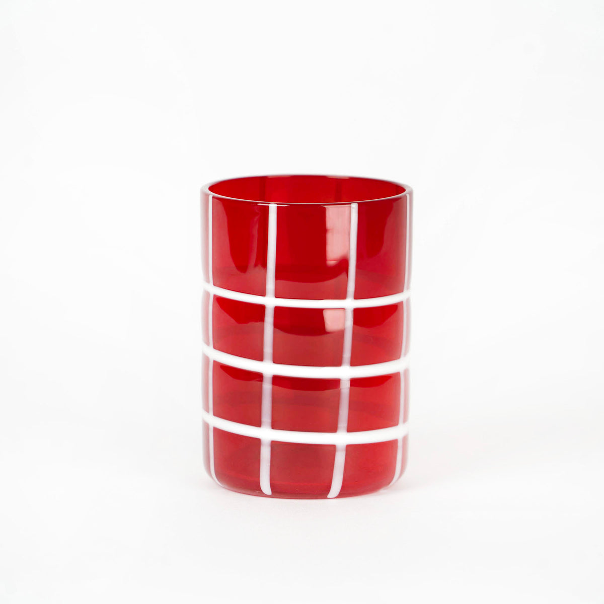 Verre rouge transparent cylindrique avec décorations en grille blanche sur fond blanc.