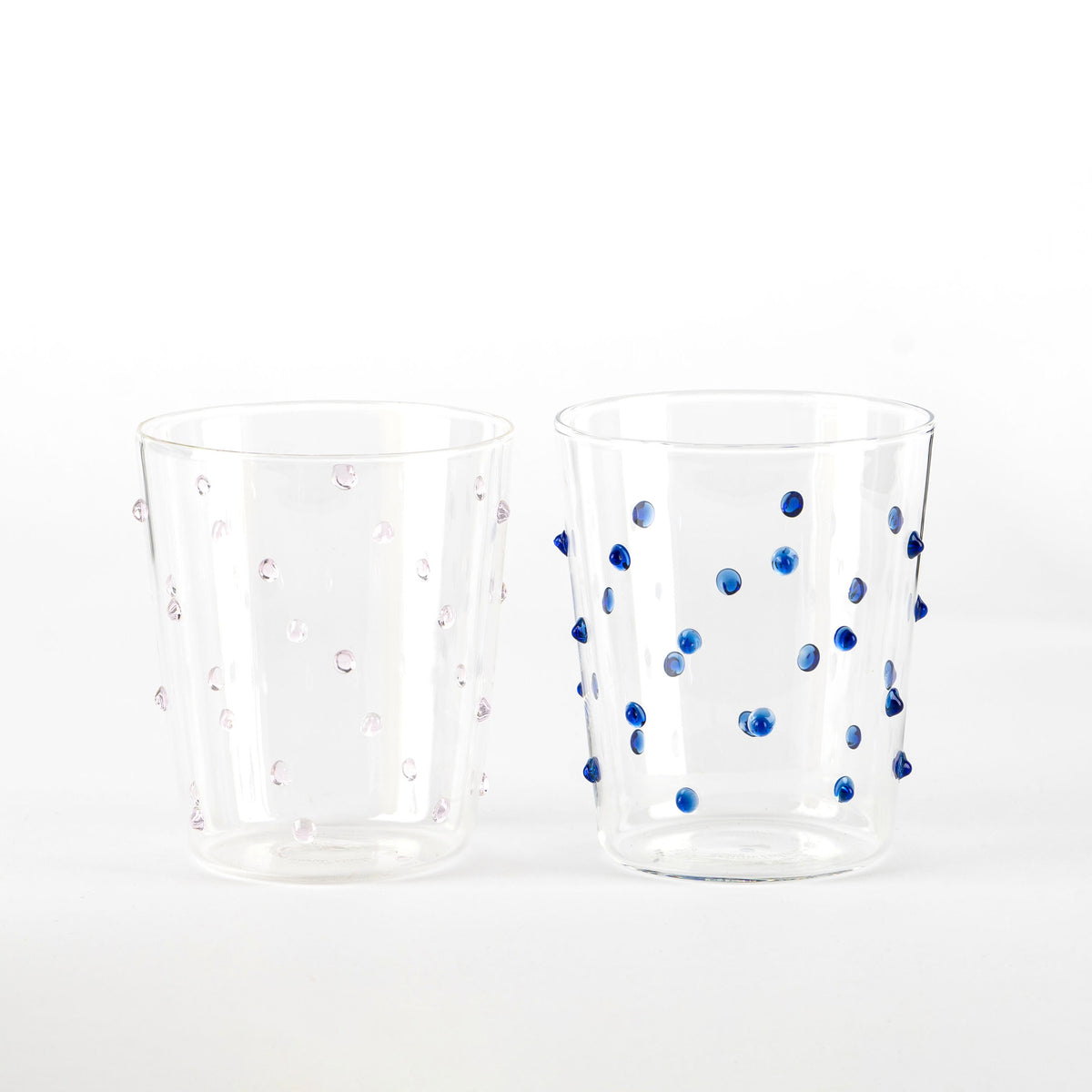 Due bicchieri trasparenti in vetro con puntini sporgenti, uno con punti rosa e l'altro con punti blu, su sfondo bianco.