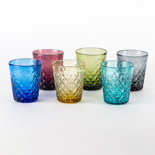 sei bicchieri di vetro trasparente sfaccettati di colori diversi disposti su fondo bianco, blu, viola, giallo, verde, turchese e grigio