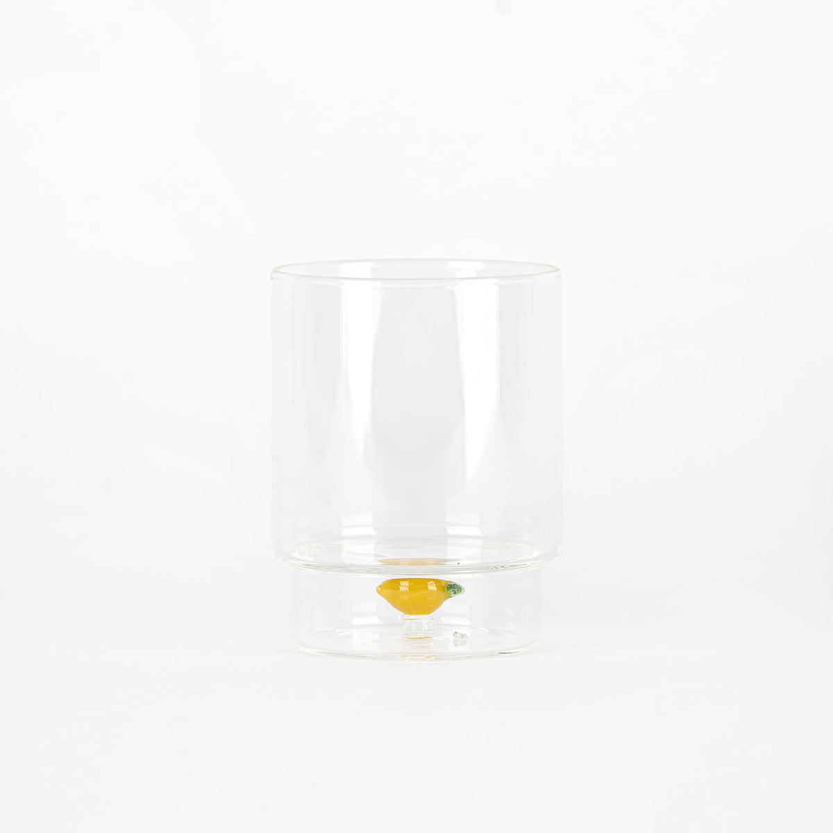 bicchiere trasparente in vetro con piccolo limone decorativo interno alla base, sfondo bianco uniforme