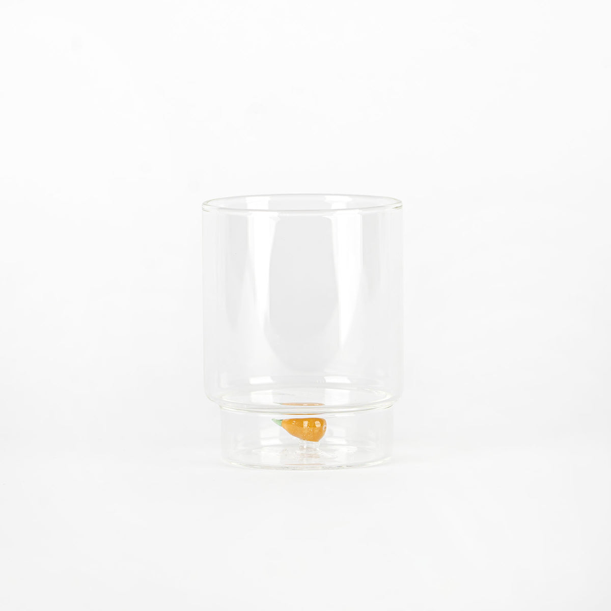 bicchiere trasparente di vetro con carota arancione decorativa sul fondo, sfondo bianco uniforme
