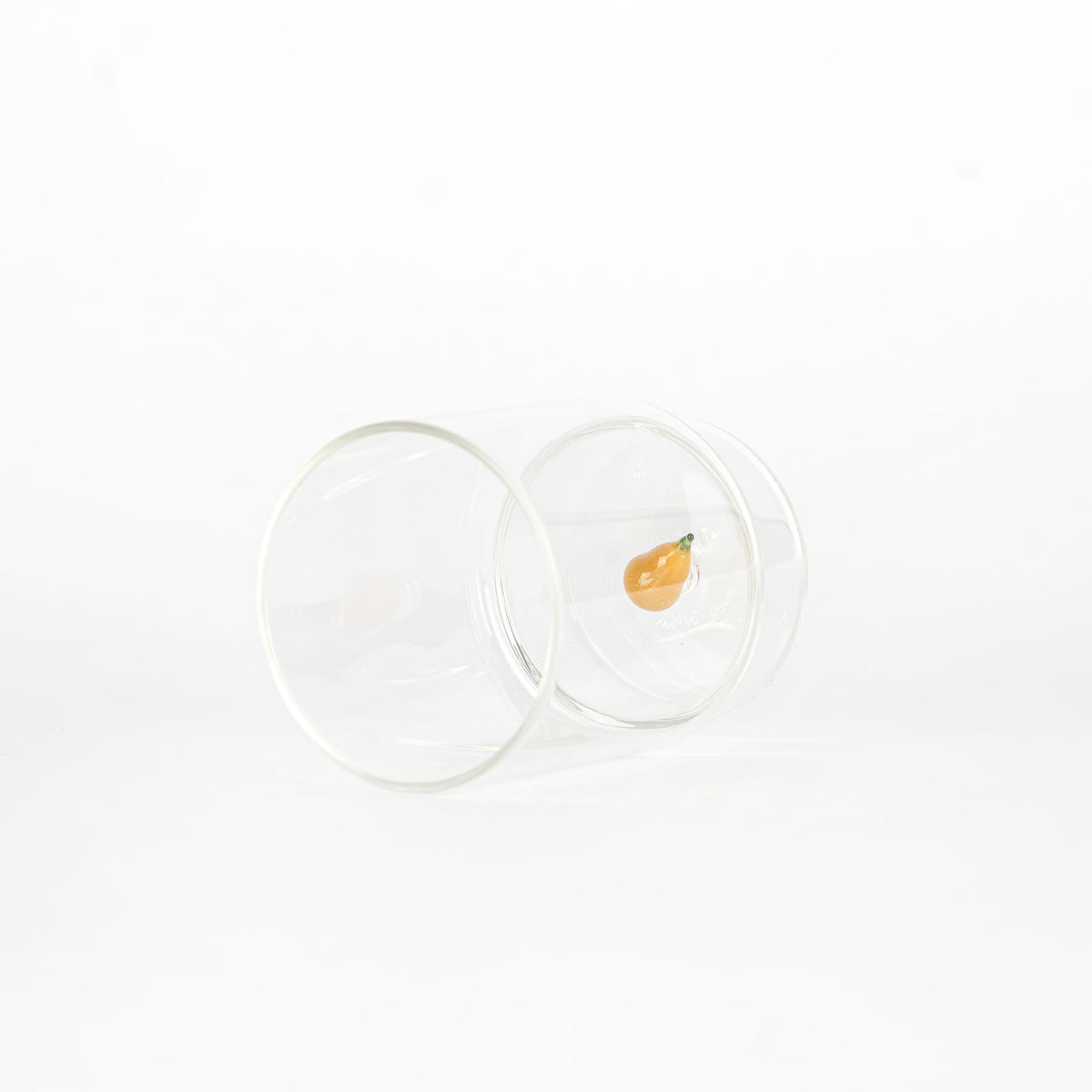 bicchiere di vetro trasparente rovesciato con piccola decorazione interna a forma di pera arancione con picciolo verde, sfondo bianco