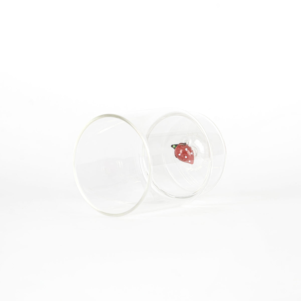 bicchiere di vetro trasparente con decorazione interna a forma di fragola rossa con puntini bianchi su sfondo bianco