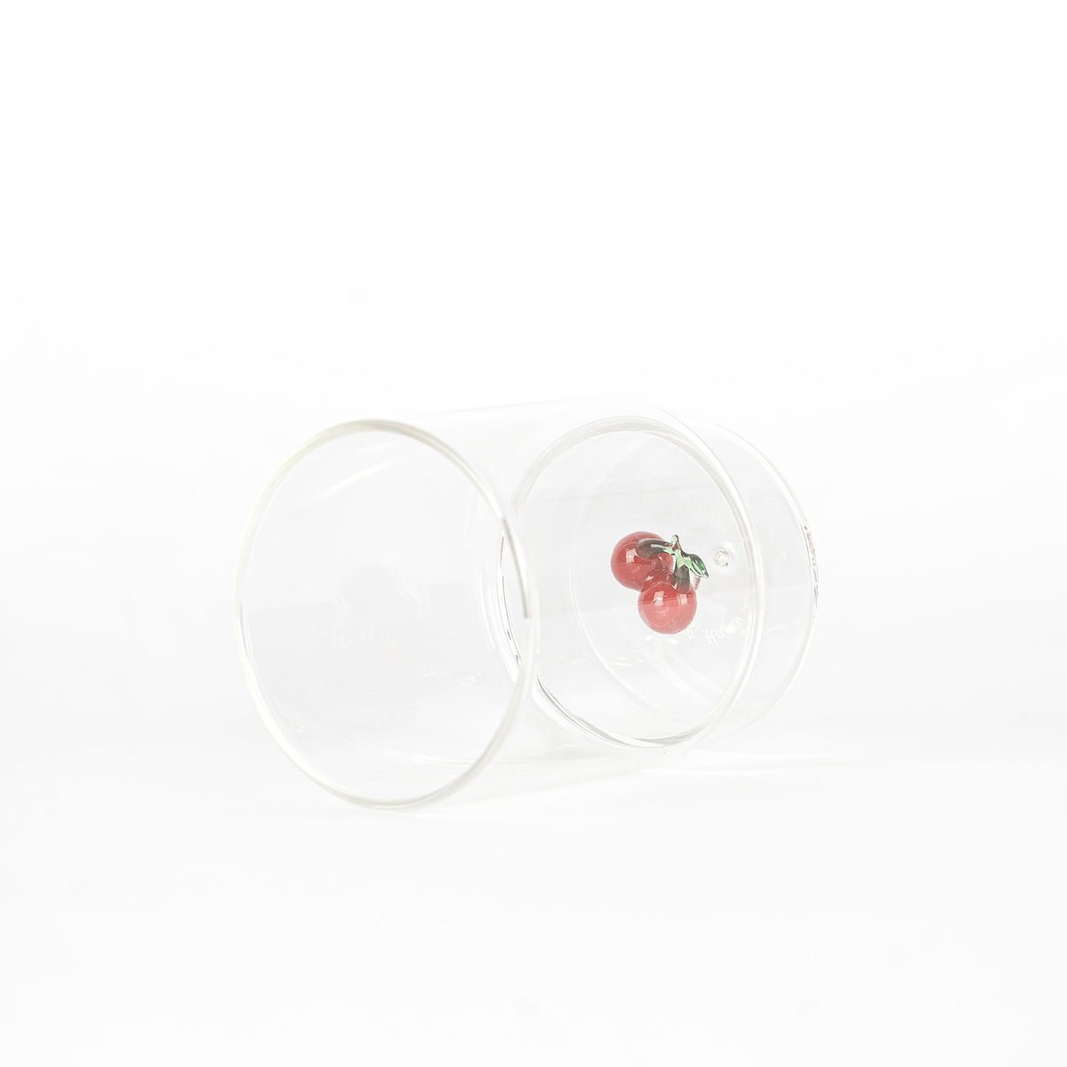bicchiere trasparente in vetro con decorazione interna di due ciliegie rosse con fogliolina verde su sfondo bianco