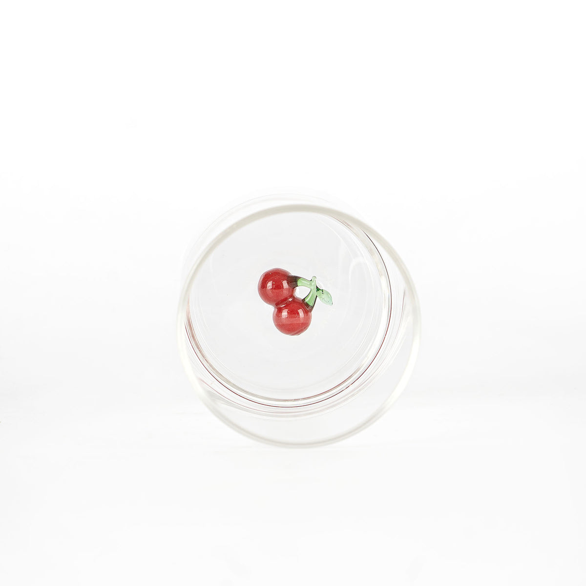 bicchiere di vetro trasparente con decorazione interna di ciliegie rosse con foglie verdi su sfondo bianco