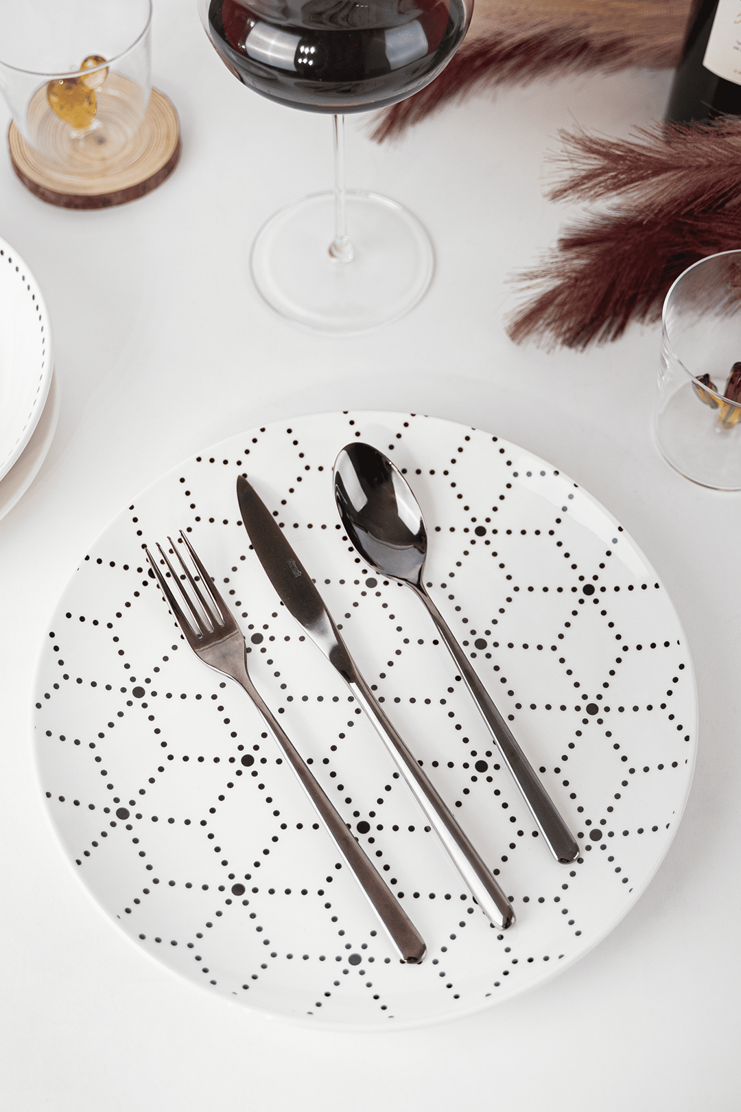 Assiette blanche avec motif géométrique noir, couverts en acier brillant: fourchette, couteau et cuillère, sur surface blanche.
