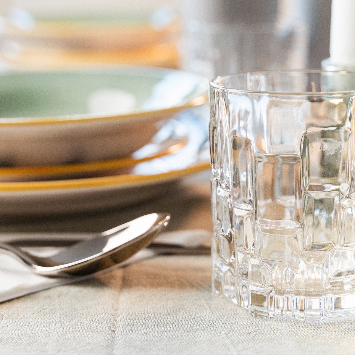 Set table with colorful ceramic plates, a transparent glass tumbler and metal cutlery.