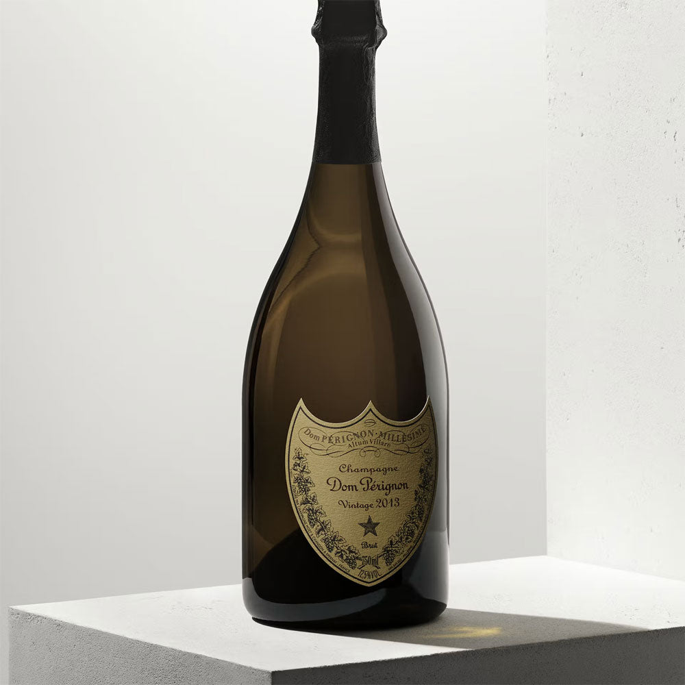 Bottiglia di champagne Dom Pérignon Vintage 2013 in vetro scuro con etichetta dorata e dettagli neri su base grigia.