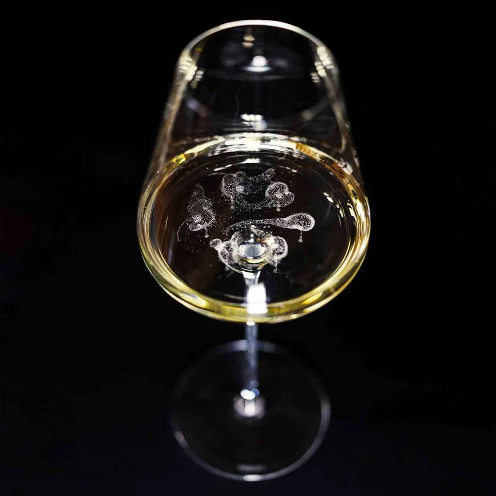 Calice di vino con liquido giallo chiaro e bollicine, su sfondo nero, con riflessi di luce sulla superficie del bicchiere.
