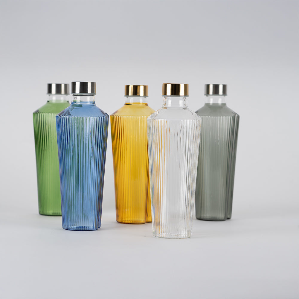 Cinco botellas de vidrio verticales con acabados a rayas en verde, azul, amarillo, transparente y gris, tapones metálicos dorados y plateados, fondo