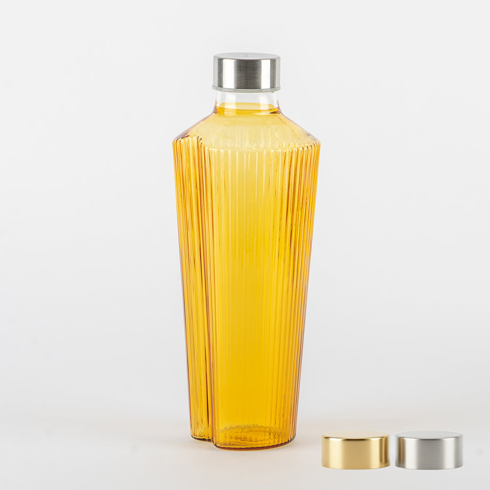 Botella amarilla de vidrio con superficies estriadas y tapón metálico plateado, con dos tapones adicionales dorado y plateado sobre fondo blanco.
