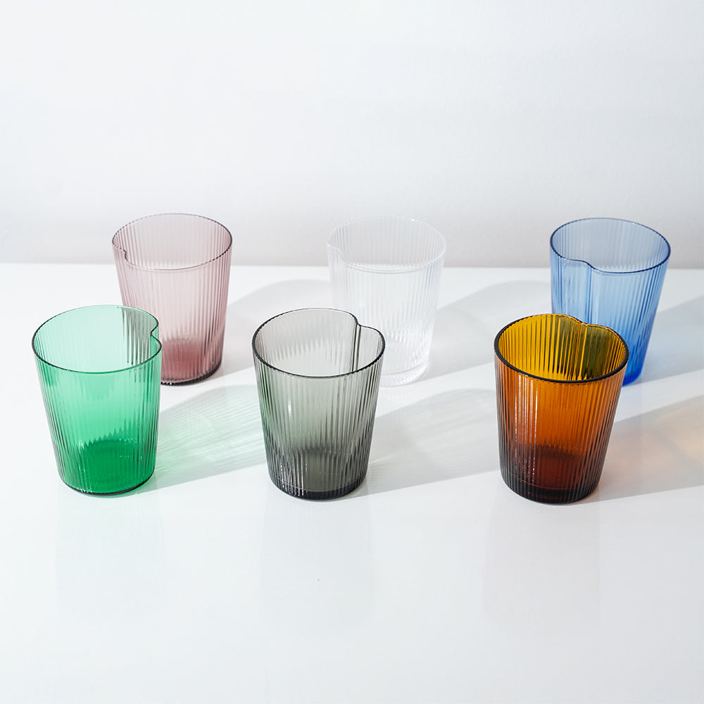 Set di sei bicchieri di vetro trasparente rigati in diversi colori: verde, rosa, grigio, bianco, blu e arancione, su superficie bianca.