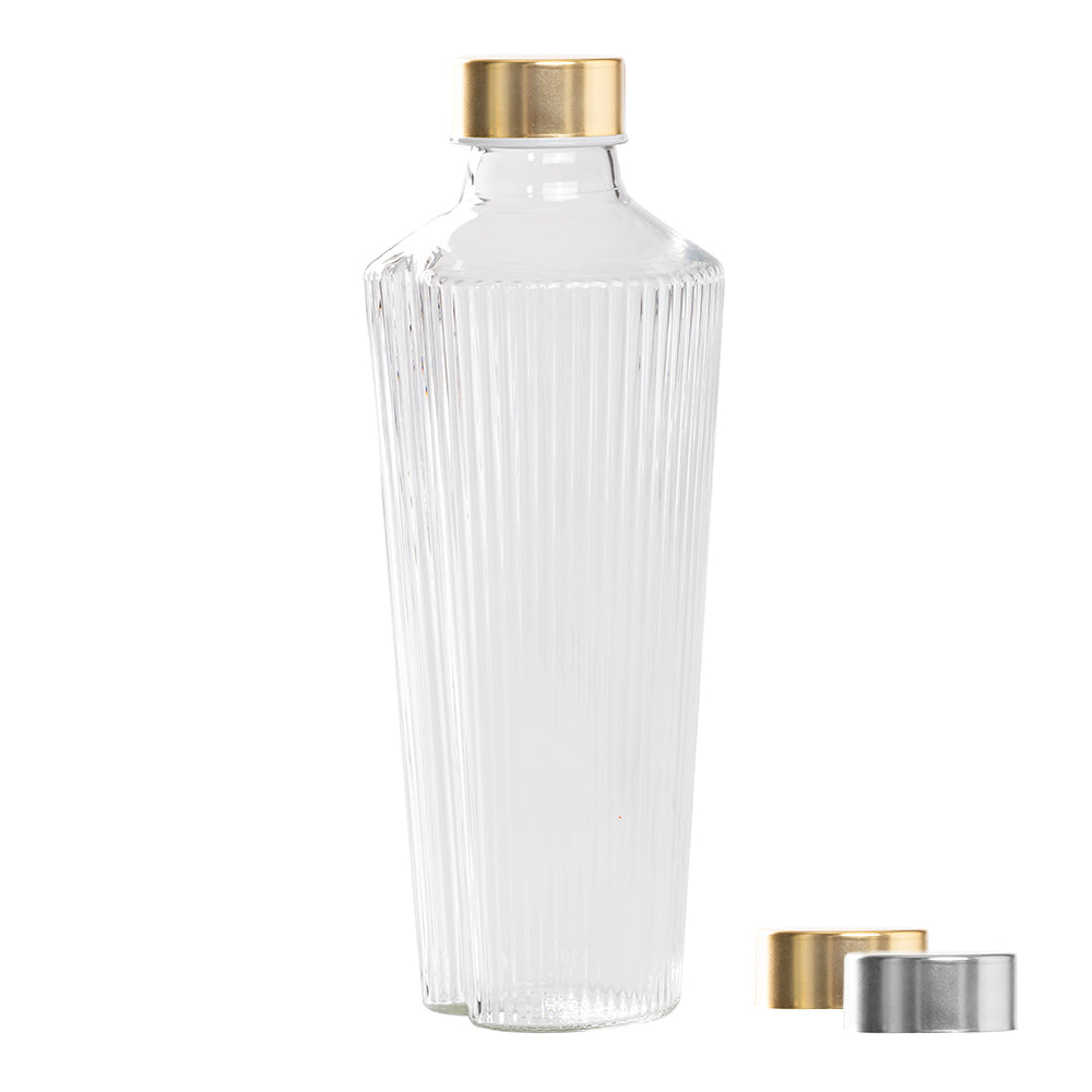 Botella de vidrio transparente con estrías verticales, tapón dorado, junto a dos tapones dorado y plateado.