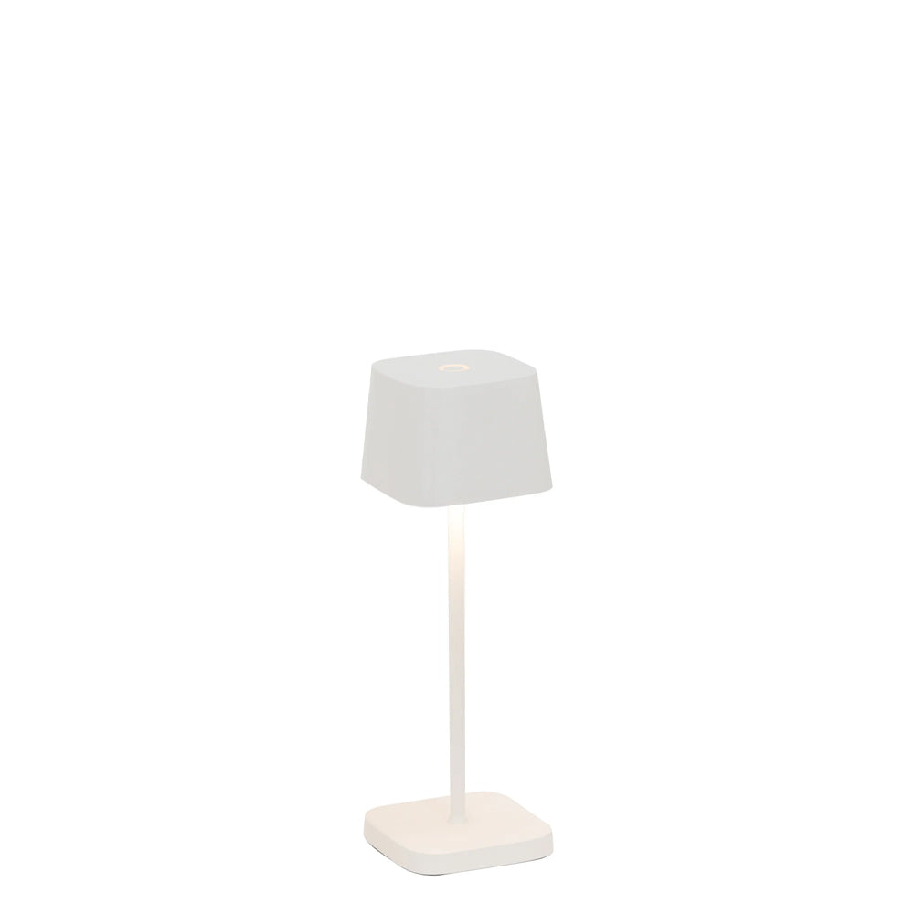 Lampe de table avec base carrée et abat-jour conique, tous deux blancs. Éclaire d'une lumière chaude et douce.