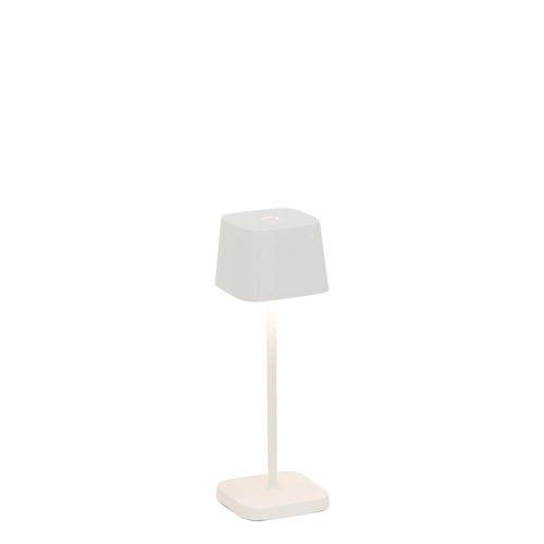 Lampada da tavolo con base quadrata e paralume a forma di cono, entrambi bianchi. Illumina con una luce calda e soffusa.