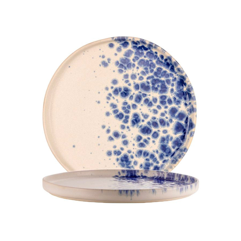 twee ronde beige keramische borden met blauwe vlekken en verlopen, één staand en één liggend, witte achtergrond