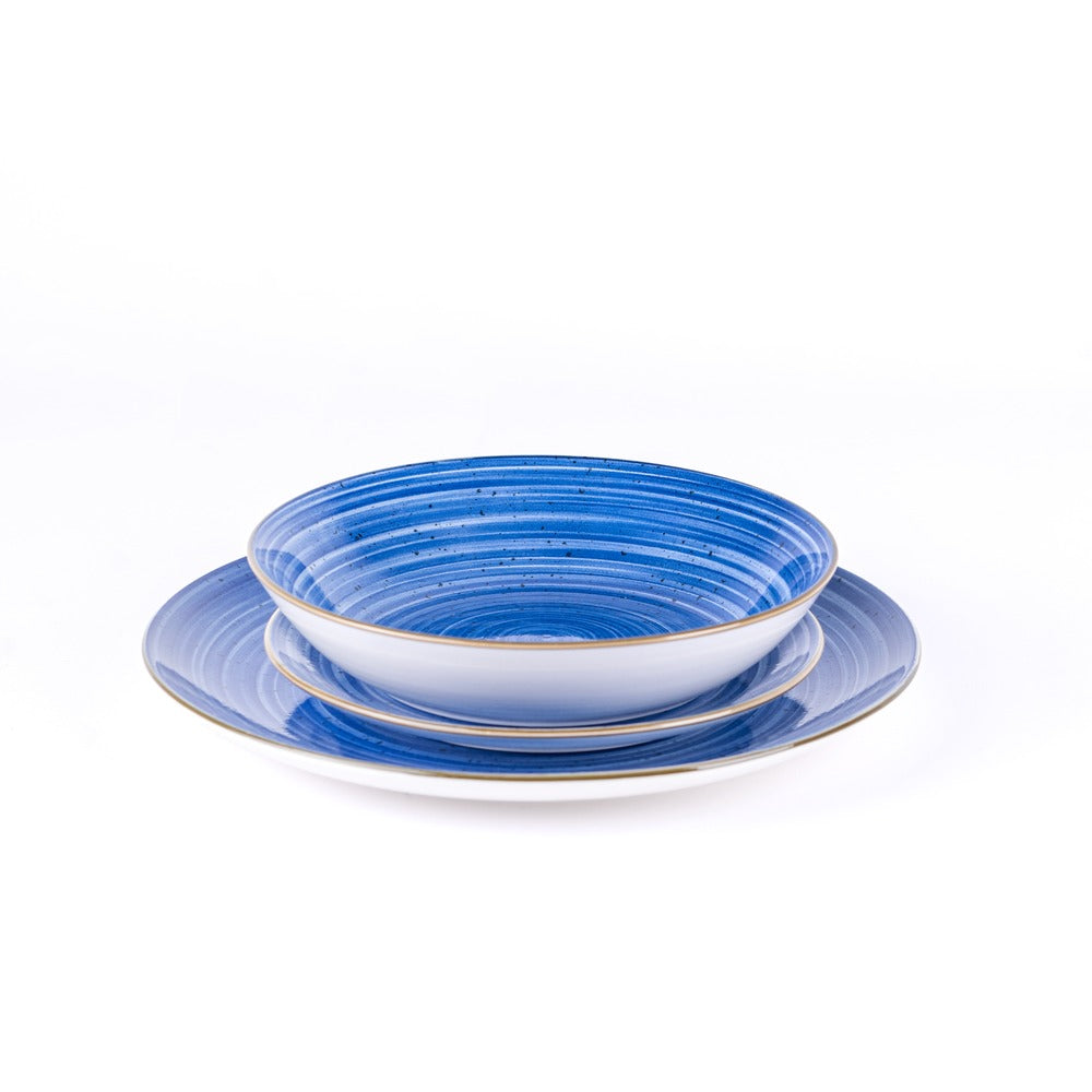 Ciotola bianca con bordo dorato e piatto blu con righe, entrambi in ceramica, posizionati uno sopra l'altro su sfondo bianco.