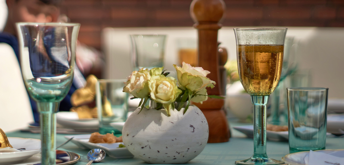 Weißes Centrepiece mit cremefarbenen Rosen, transparenten grünen Gläsern und gedecktem Tisch im Freien