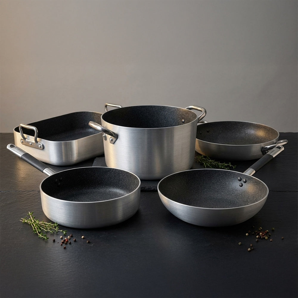 Set de ollas de acero inoxidable, con acabado mate y revestimiento interior negro. Presentes dos sartenes y una cacerola.