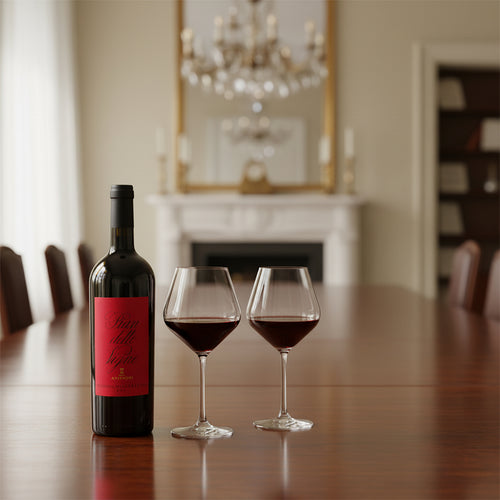 Bottiglia di vino rosso con etichetta rossa e due bicchieri con vino su tavolo di legno davanti a camino e specchio in ambiente elegante