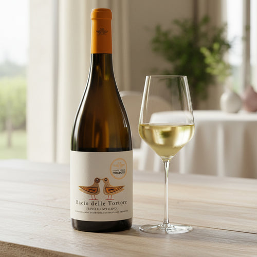 Bottiglia di vino Bianco Bacio delle Tortore con etichetta beige e disegno di due tortore, accanto calice trasparente con vino bianco, su tavolo di
