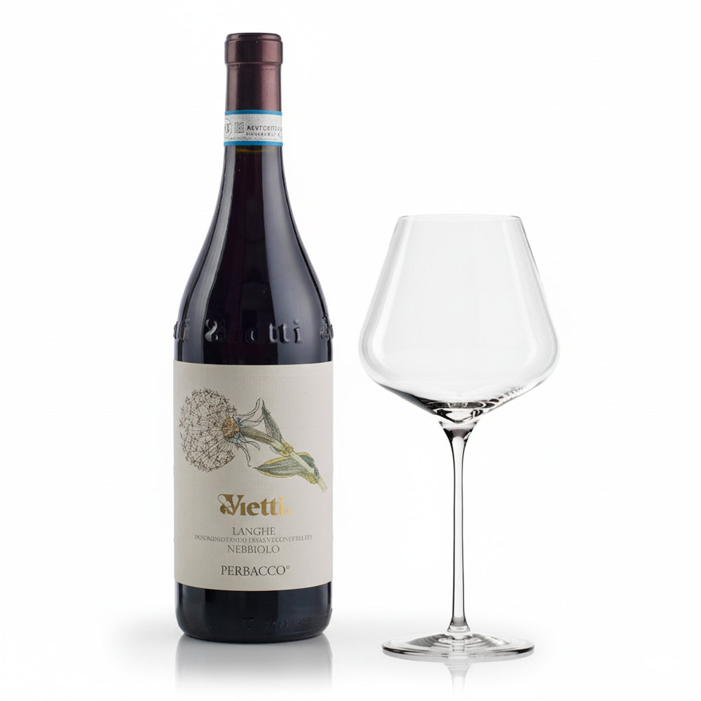 Vietti Langhe Nebbiolo Perbacco red wine bottle with beige label and flower design and clear wine glass beside on white background.