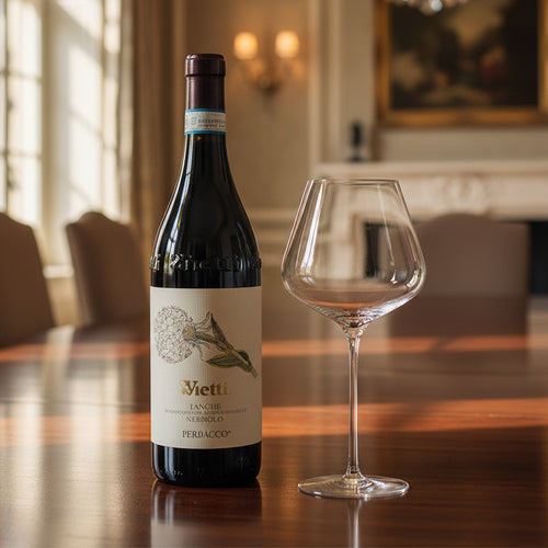 Bouteille de vin rouge Vietti Langhe Nebbiolo Perbacco avec étiquette blanche et calice en verre transparent sur table en bois en intérieur élégant.