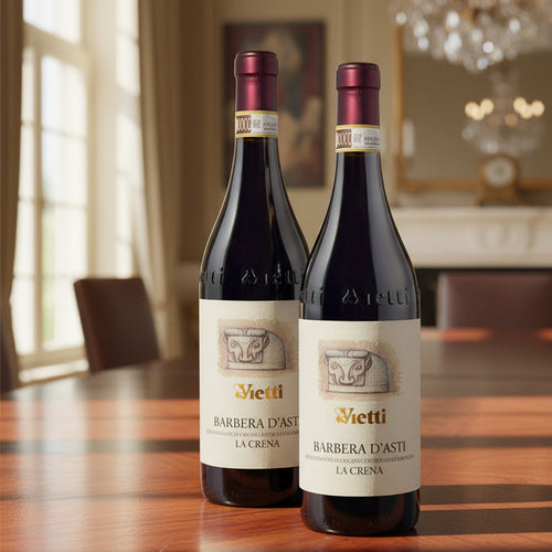 Deux bouteilles de vin rouge Vietti Barbera d'Asti La Crena avec étiquettes beige, bouchon bordeaux, sur table en bois en intérieur élégant.