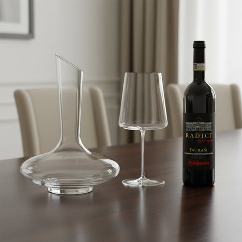 Caraffa di vetro trasparente, calice da vino con stelo sottile e bottiglia di vino rosso Radici Taurasi su tavolo in legno, sfondo soggiorno elegante.