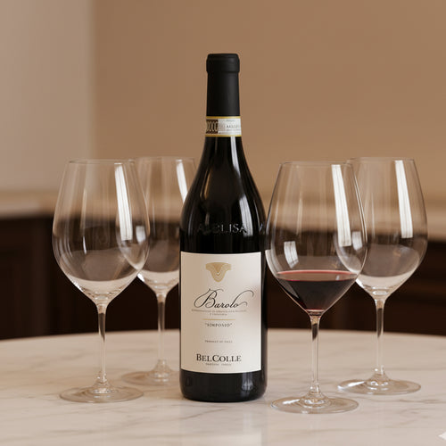Bouteille de vin rouge Barolo Belcolle avec quatre calices en verre transparent, un partiellement rempli, sur table en marbre blanc.