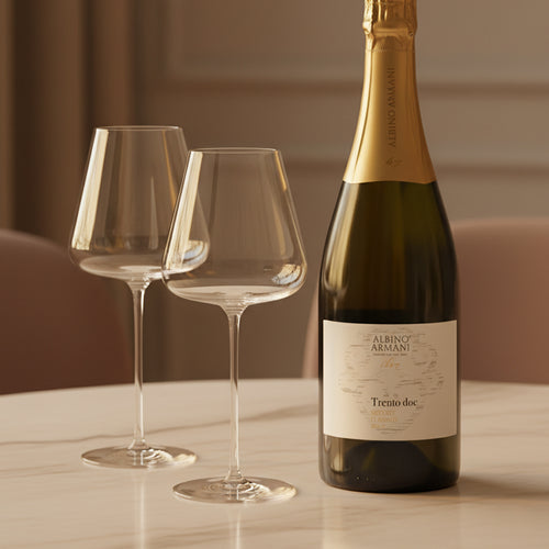 Bouteille de vin Albino Armani Trento DOC avec bouchon doré et deux calices en verre transparent sur table en marbre blanc.