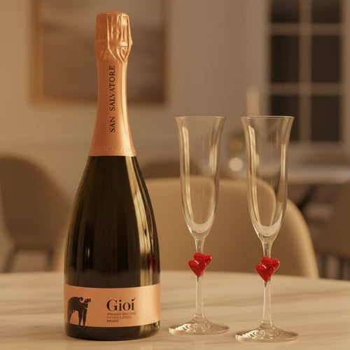 Bouteille de spumante Gioì San Salvatore avec étiquette rose or et deux flûtes en verre avec décorations en forme de cœur rouge sur table blanche dans