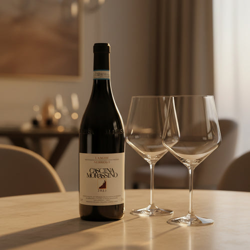 Bouteille de vin rouge Cascina Morassino 2023 sur table claire avec deux calices en verre transparent vides en intérieur lumineux.