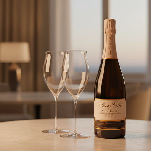 Bouteille sombre de vin mousseux Pietro Colla Alta Langa Extra Brut à côté de deux calices transparents sur table claire, intérieur avec lampe floue.