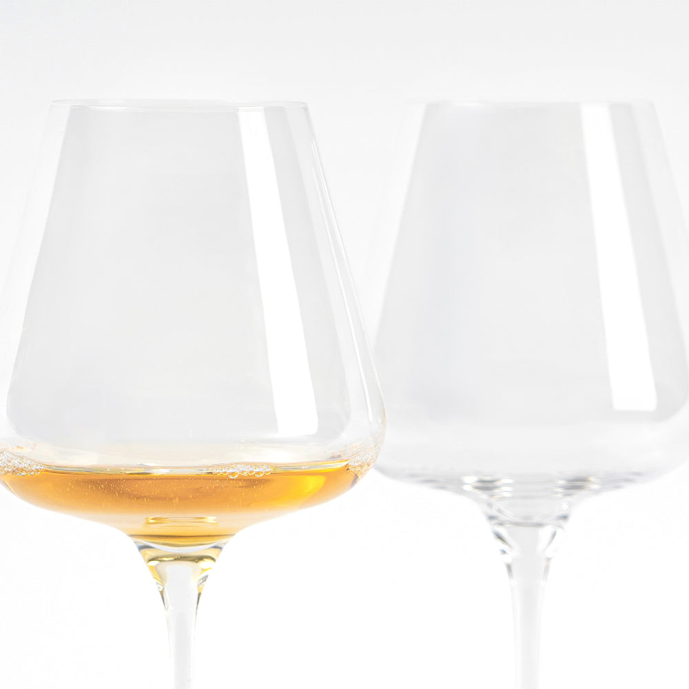 Due calici di vetro trasparente, uno con liquido dorato e bollicine. Sfondo chiaro e semplice.