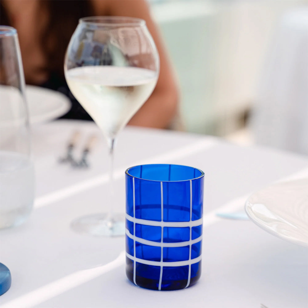 Blue verre en verre en verre avec white grid pattern sur white table à côté de tigemed glass of vin blanc et white plate in bright indoor setting.