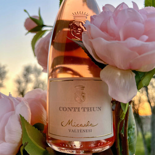 CONTI THUN Micalea Valtènesi Roséweinflasche aus transparentem Glas mit beigefarbenem Etikett und goldenen Details, umgeben von rosa Rosen