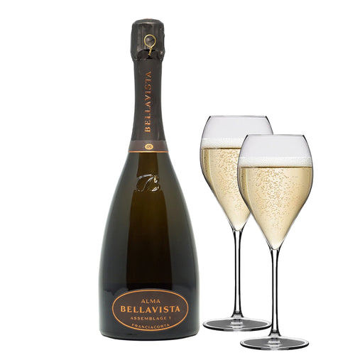 Bottiglia di spumante Bellavista Alma Assemblage 1 Franciacorta color ambrato con due flute trasparenti colmi di bollicine, sfondo bianco.