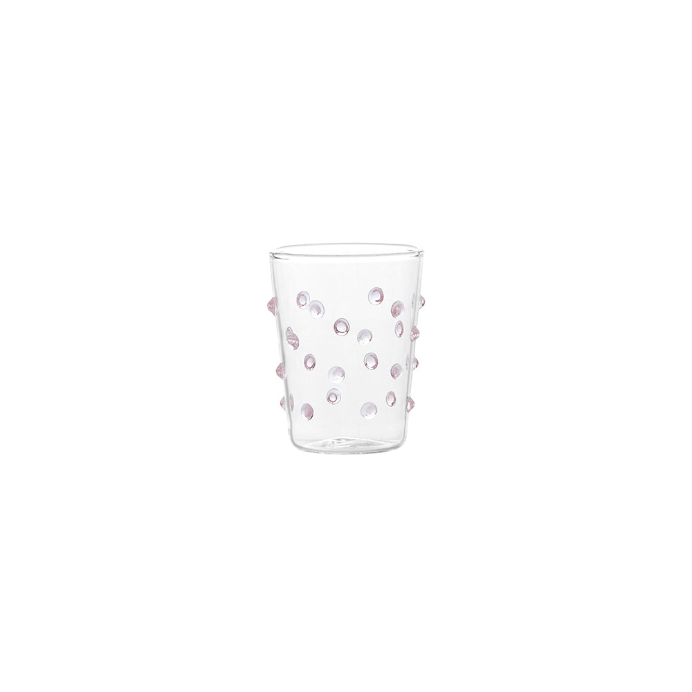 Verre transparent en verre avec décorations en relief rondes de couleur rose sur fond blanc.