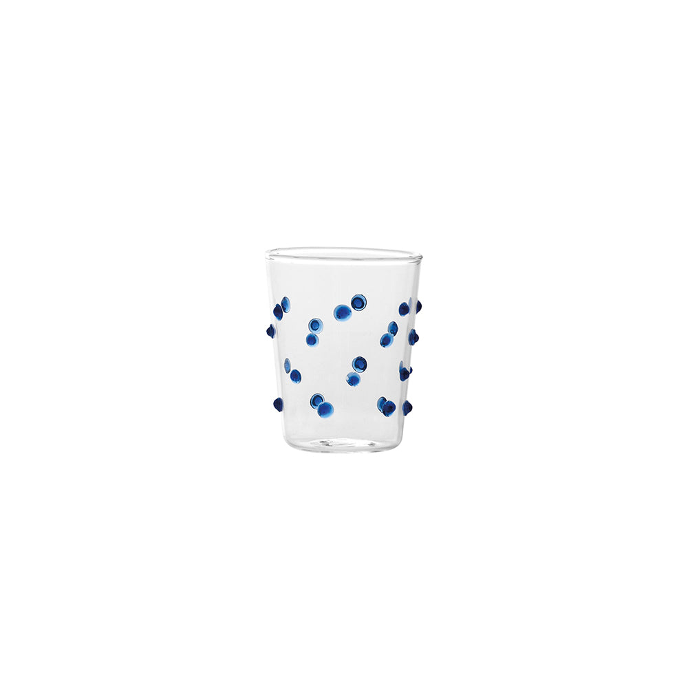 Verre transparent en verre avec décorations bleues à pois convexes distribuées sur la surface, fond blanc.