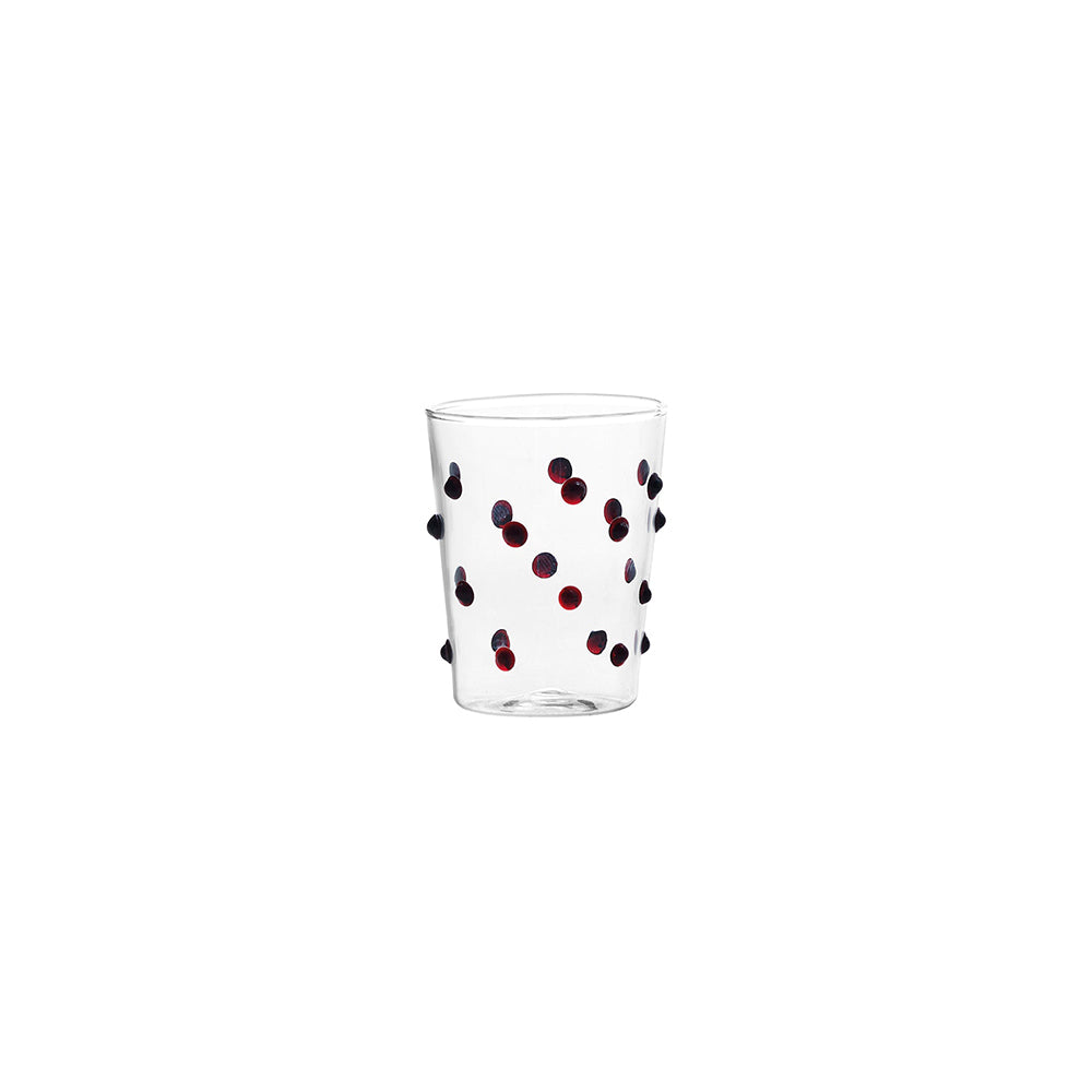 Verre transparent en verre avec petits points décoratifs rouges et noirs sur fond blanc.