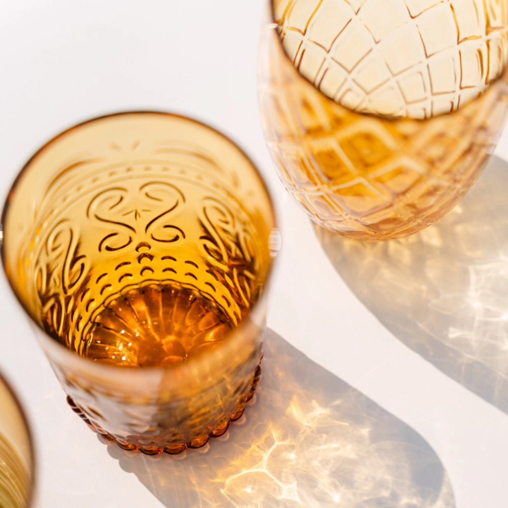 Glazen van amberkleurig glas met gegraveerde decoraties, transparant, van bovenaf op lichte achtergrond met lichtreflecties.