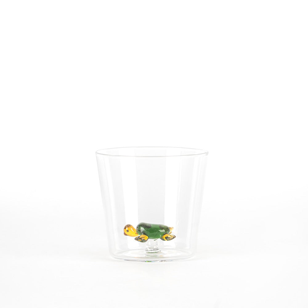 Taza transparente con una tortuga de cristal verde y amarilla en el interior, sobre fondo blanco.