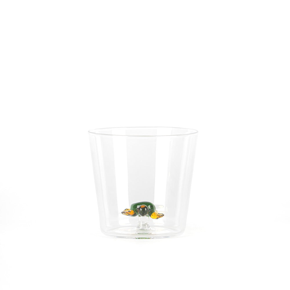 Un vaso transparente con una decoración en forma de tortuga de colores, verde y amarilla, posicionada en el centro.