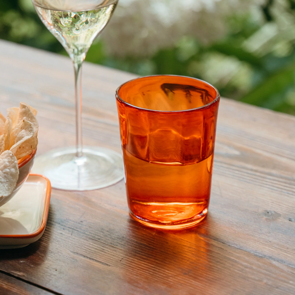 transparant oranje glazen beker met water op houten tafel, naast wijnglas en kelk met chips