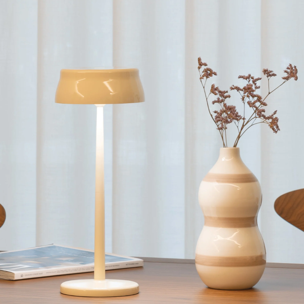 Lampe de table en métal couleur ivoire avec abat-jour rond, vase en céramique ivoire à bandes beiges et fleurs séchées, table en bois.