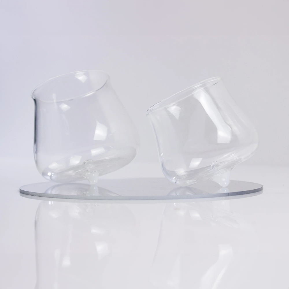 twee schuin staande transparante glazen met afgeronde basis op wit reflecterend oppervlak