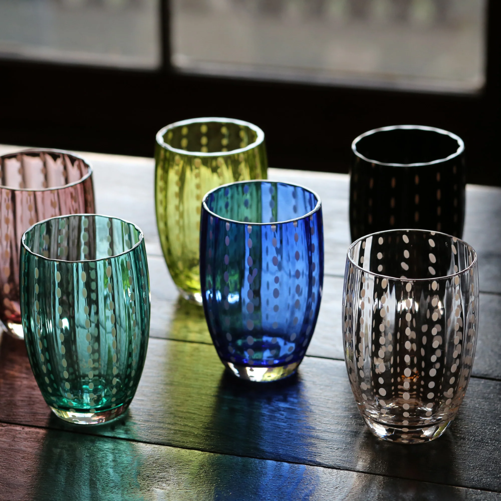 zes gekleurde glazen bekers met wit stippenpatroon, op houten tafel voor raam, kleuren groen, blauw, geel, roze en zwart